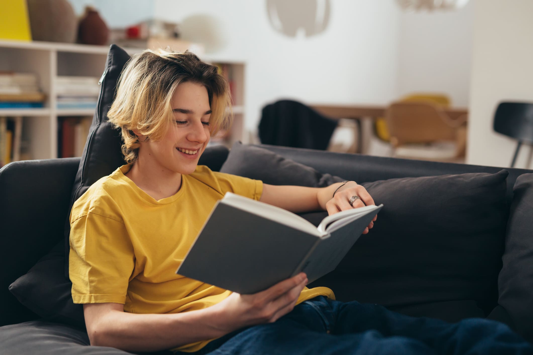 Person reading book on a sofa, smiling.