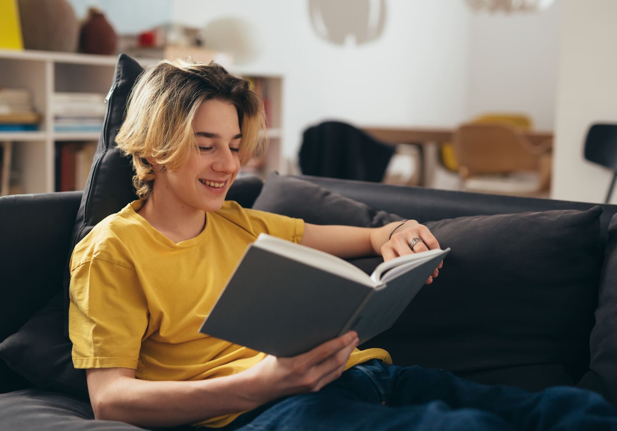 Person reading book on a sofa, smiling.